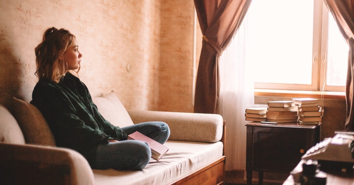 Woman looking bored with a book on her lap on a couch; what is the sin of sloth?