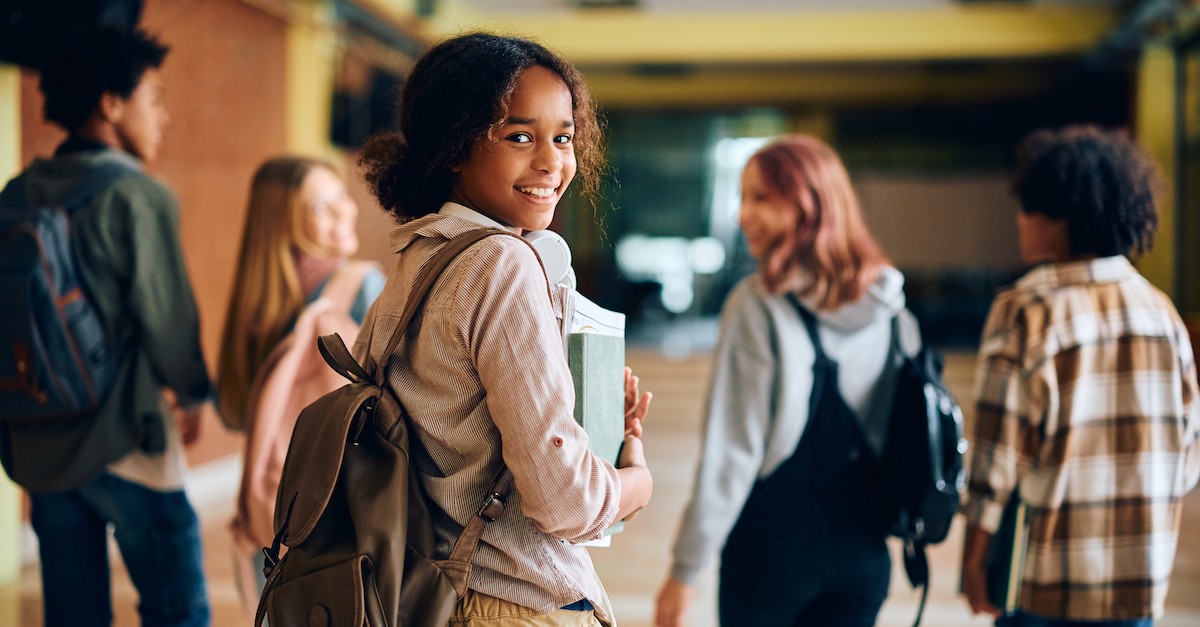 teenagers at school walking down hall with one teen turning and smiling at camera