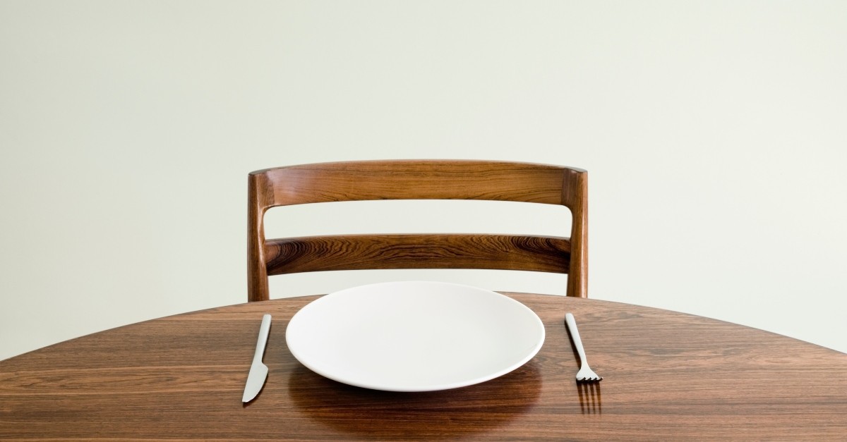 An empty dinner plate in front of an empty chair